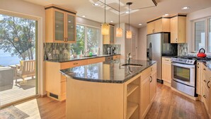 A modern kitchen with a large island, wooden cabinets, stainless steel appliances, and a view of the outdoors. - Hike, Bike & Explore: Oceanfront Kingston Getaway (Kingston)
