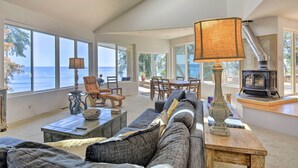 A spacious living room with a large window overlooking the sea, a cozy sofa, a wooden coffee table, and a fireplace. - Hike, Bike & Explore: Oceanfront Kingston Getaway (Kingston)