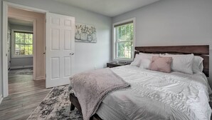 Quarto com uma cama grande, uma porta que dá para outro cômodo e uma janela com vista para árvores.