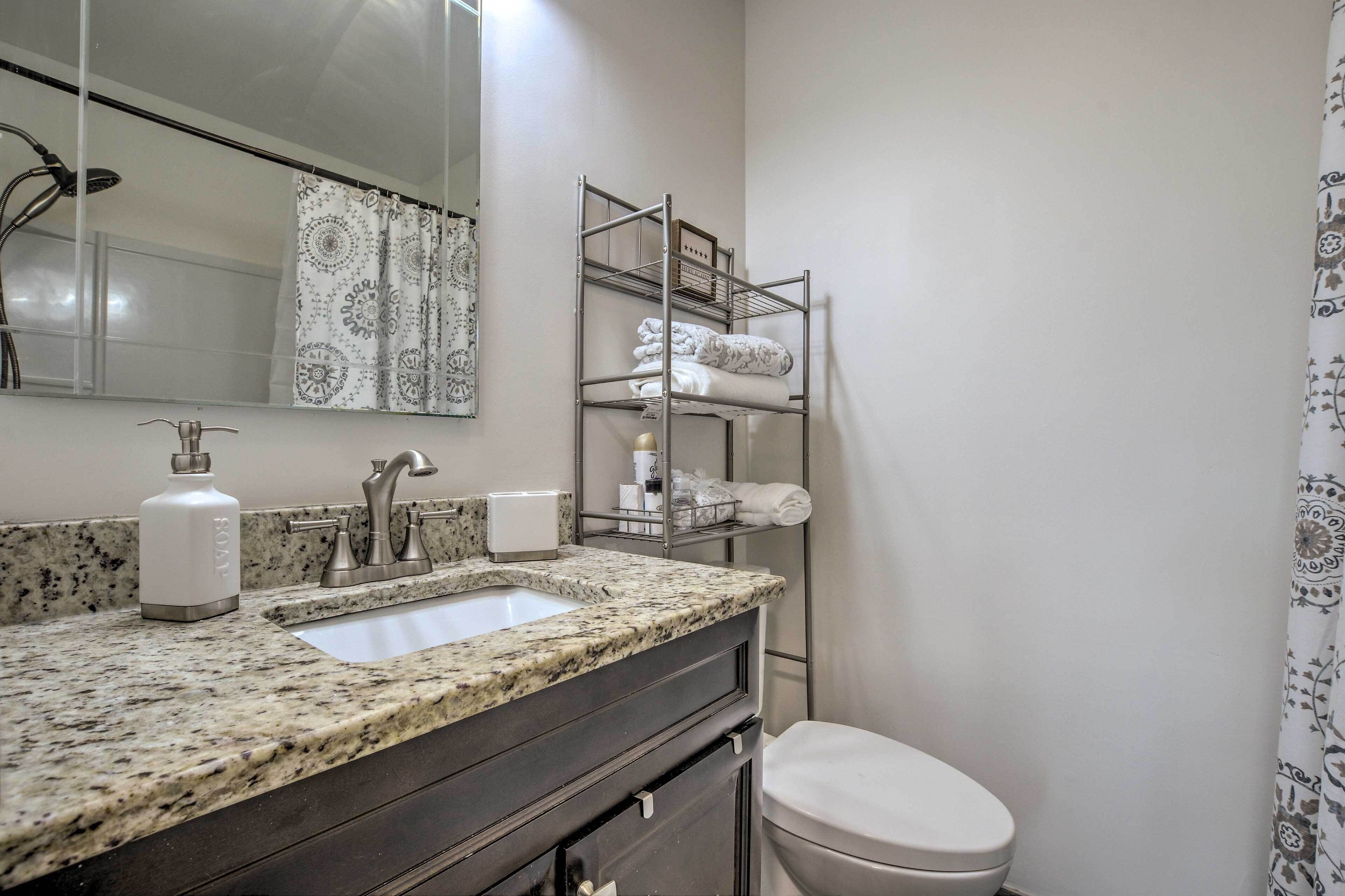 A bathroom with a granite countertop sink, a mirror, a shower, and a toilet.