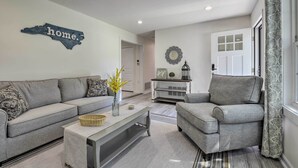 Sala de estar com sofá cinza, poltrona cinza, mesa de centro e um objeto decorativo na parede.