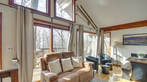 A spacious living area with a brown leather sofa, a wooden dining table, and a black chair. Large windows provide a view of the outdoors. - Cozy 'hillside Hideaway' in Wintergreen Resort! (Roseland)
