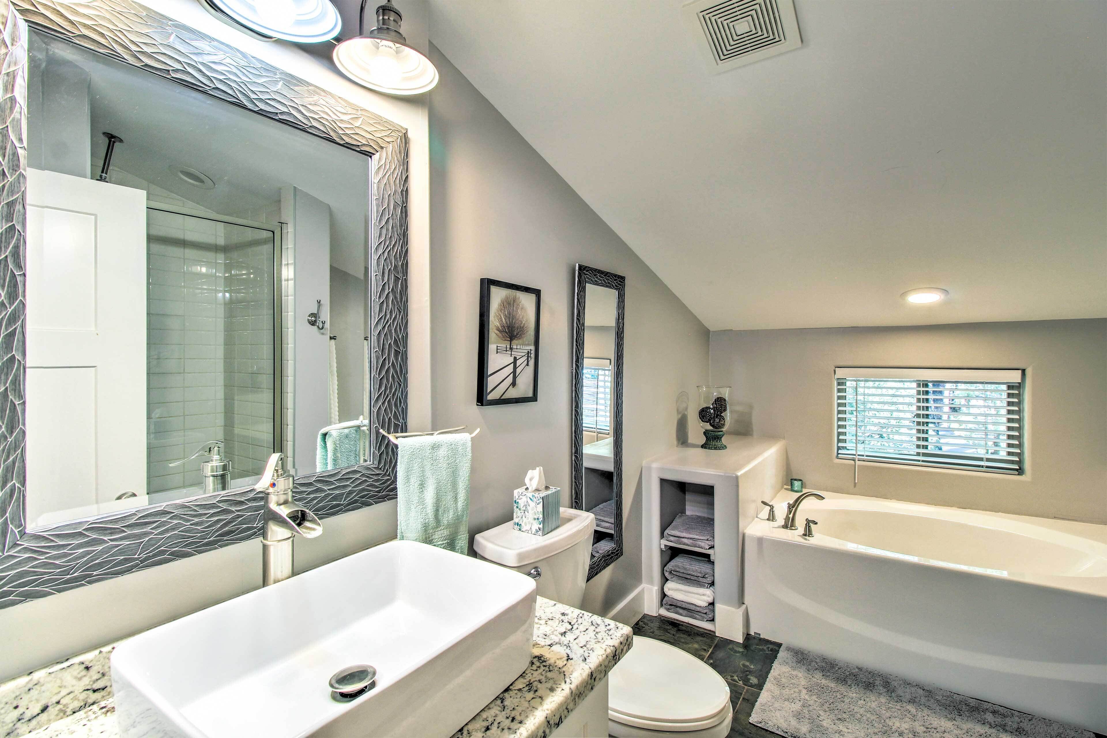 A modern bathroom with a large mirror, a bathtub, a toilet, and a sink.
