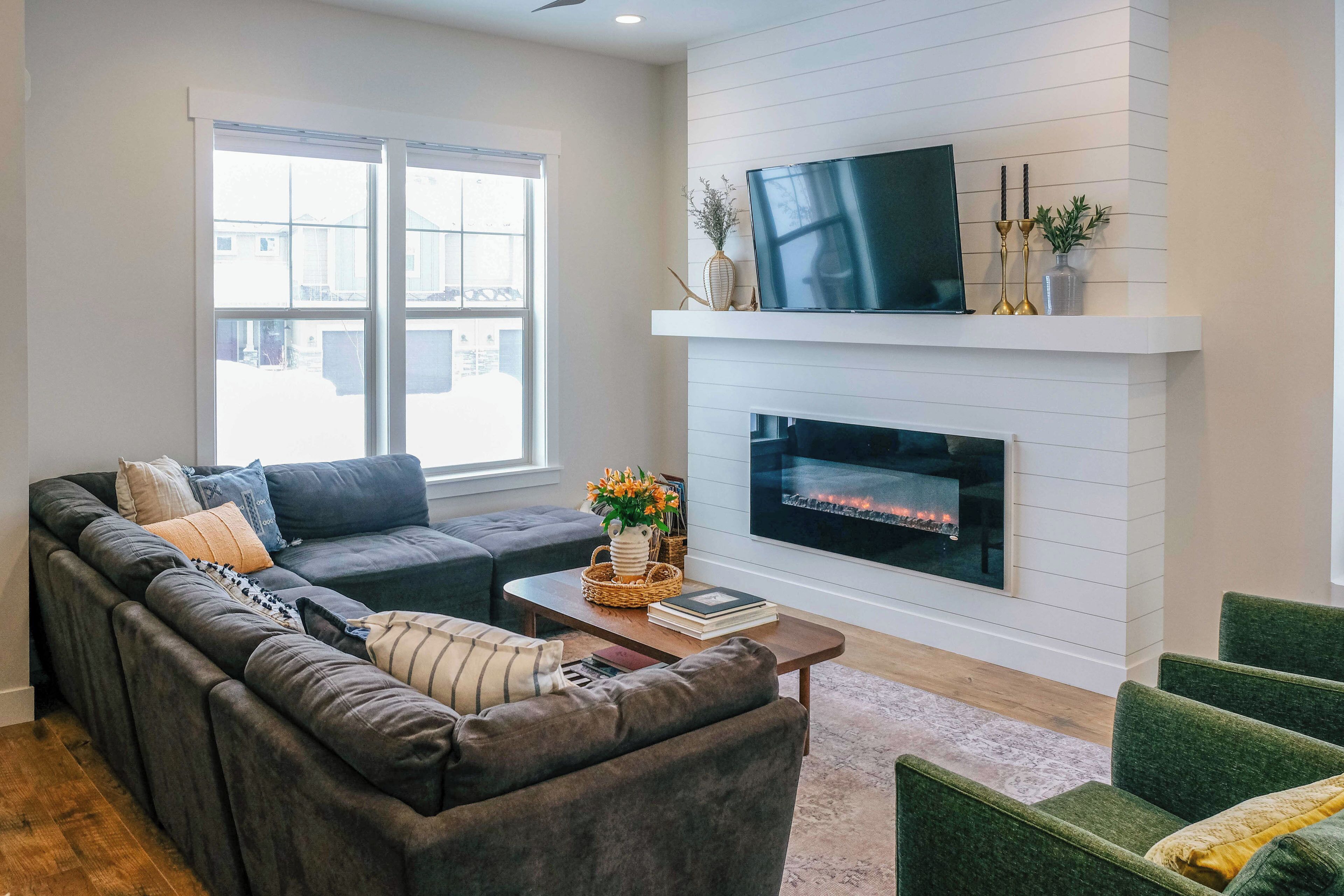 A living room with a sectional sofa, a fireplace, a flat-screen TV, and a large window.