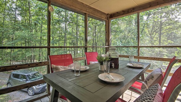 A dining area with a table set for two, large windows, and a view of a forest. - Mountain Town Adventures Home w/ Fire Pit! (Fort Valley)
