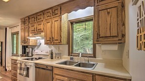 A kitchen with wooden cabinets, a double sink, and a window with a view of greenery. - Mountain Town Adventures Home w/ Fire Pit! (Fort Valley)