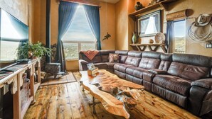 A cozy living room with a leather sofa, a wooden coffee table, and a television. - Mtn-view Adobe Home w/ Large Deck Near Prescott! (Mayer)