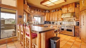 A spacious kitchen with wooden cabinets, a large island, and a view of the outdoors. - Mtn-view Adobe Home w/ Large Deck Near Prescott! (Mayer)