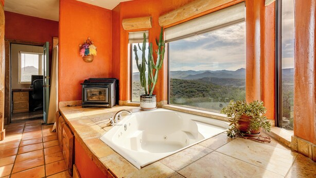 A bathroom with a large bathtub, a window with a view of mountains, and a cactus plant on the windowsill. - Mtn-view Adobe Home w/ Large Deck Near Prescott! (Mayer)