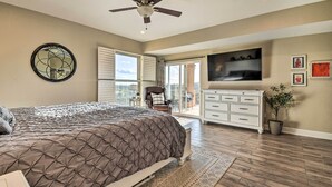 Un dormitorio con cama, ventilador de techo, televisor, cómoda y vista al exterior.