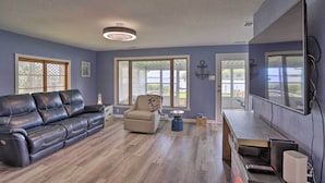 A living room with a black leather sofa, a beige armchair, and a wooden coffee table. - Lake Erie Waterfront Home w/ Sunroom & Yard! (Erie)