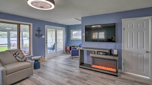 A living room with a fireplace, a sofa, a TV, and a ceiling fan. - Lake Erie Waterfront Home w/ Sunroom & Yard! (Erie)