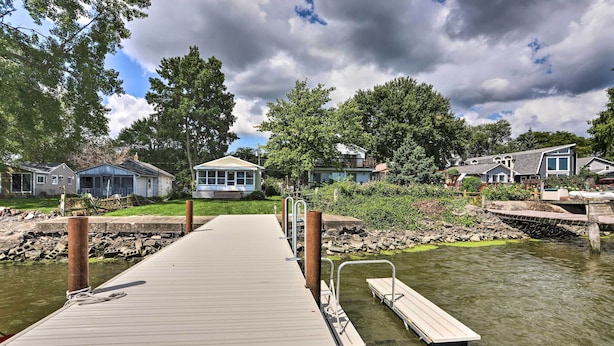 A wooden dock leading to a calm water body with houses in the background. - Lake Erie Waterfront Home w/ Sunroom & Yard! (Erie)