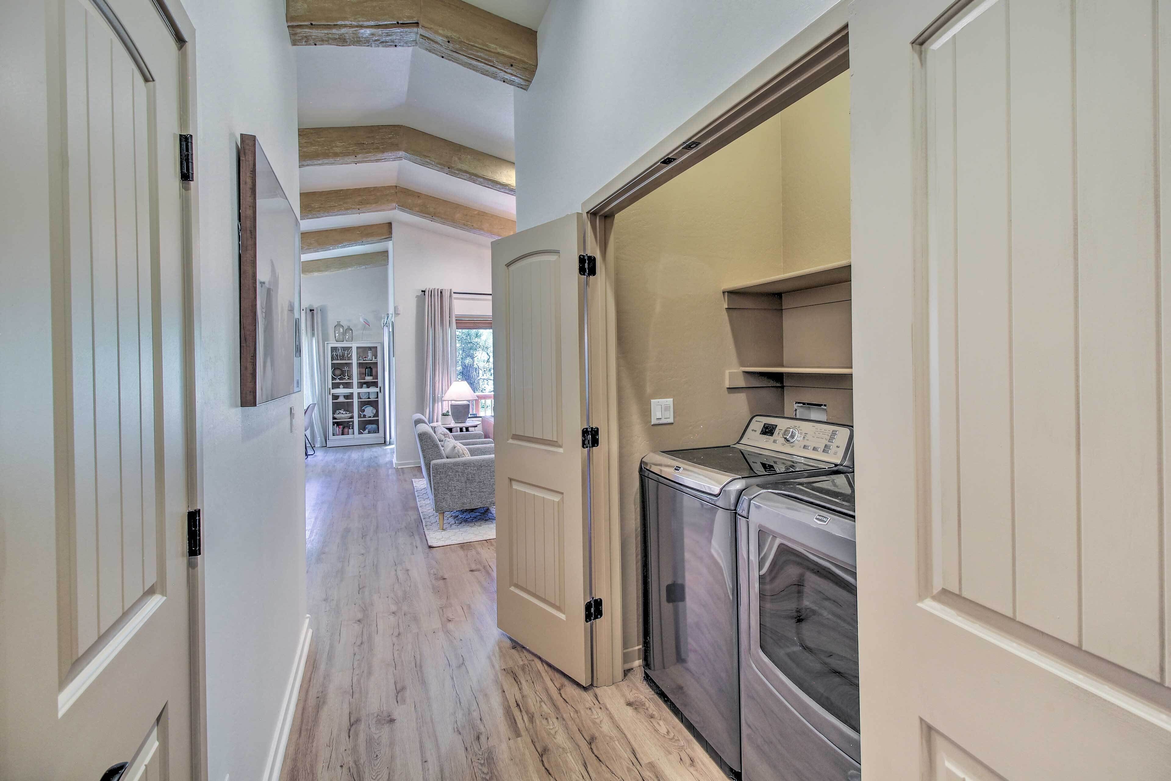 A hallway with wooden floors, a laundry area with a washer and dryer, and a door leading to a living room with a sofa and a coffee table.