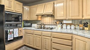 A kitchen with wooden cabinets, a black refrigerator, a stove, and various kitchen utensils. - Duck Creek Village Cabin w/ Deck on Half Acre (Duck Creek Village)