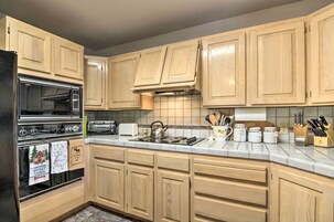 A kitchen with wooden cabinets, a black refrigerator, a stove, and various kitchen utensils.
