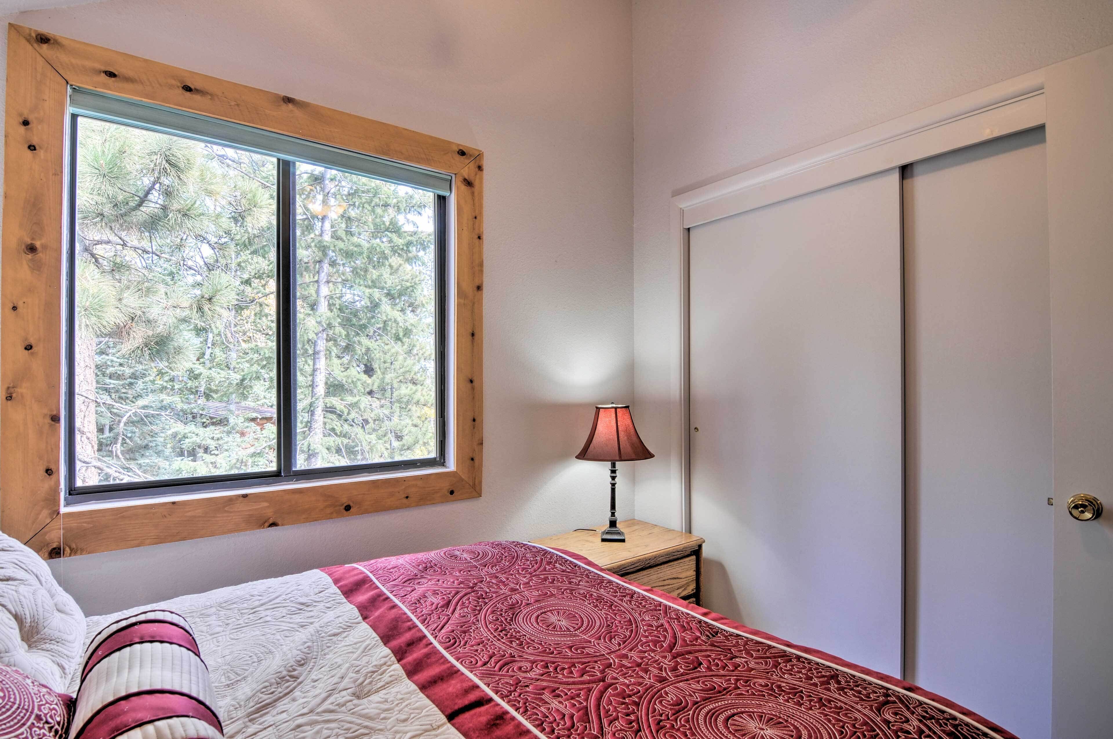 A bedroom with a large window, a bedside table with a lamp, and a wardrobe.