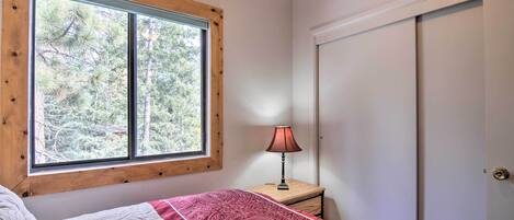 A bedroom with a large window, a bedside table with a lamp, and a wardrobe.