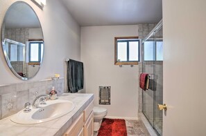 A bathroom with a large mirror, a double sink, a toilet, and a glass shower enclosure. - Duck Creek Village Cabin w/ Deck on Half Acre (Duck Creek Village)
