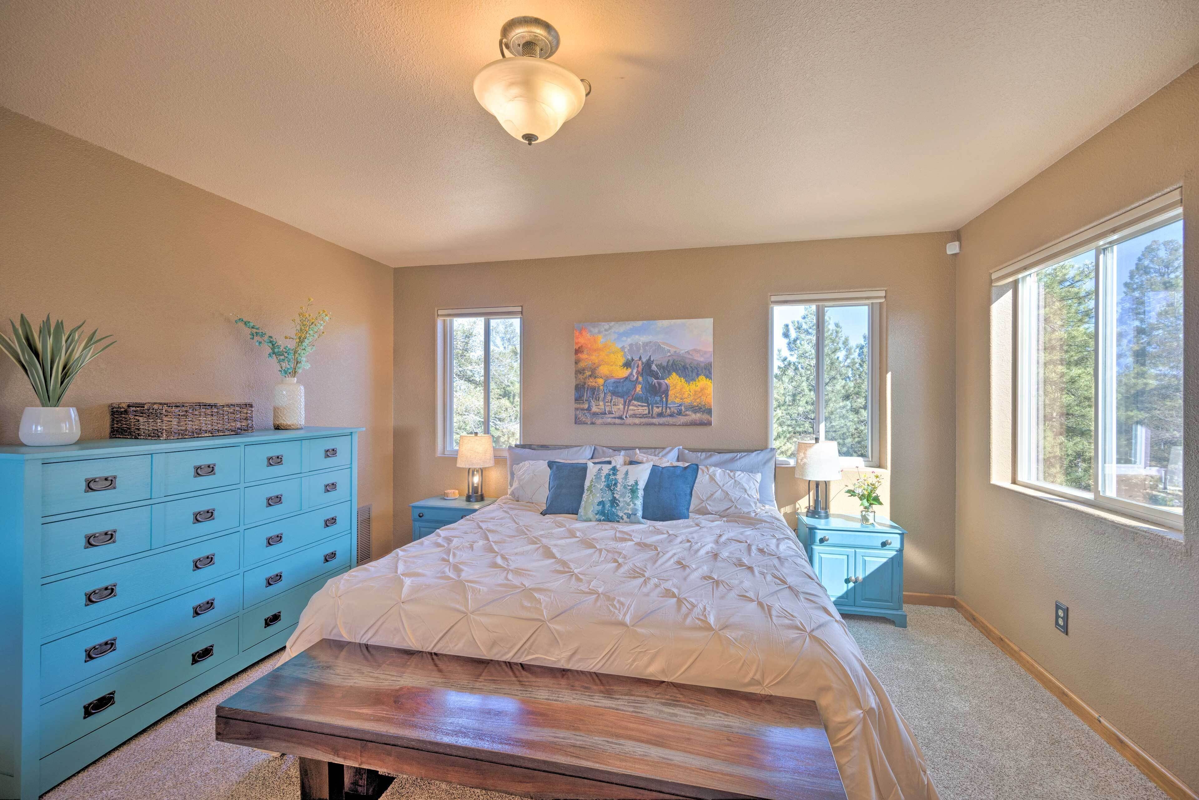 A bedroom with a large bed, a blue dresser, a bench, and two nightstands with lamps.