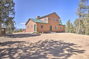 A two-story house with a green roof, surrounded by trees and a clear sky.