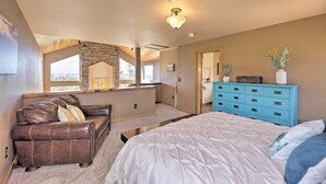 Une chambre avec un grand lit, un canapé en cuir marron, une commode bleue et un mur d’accent en pierre.