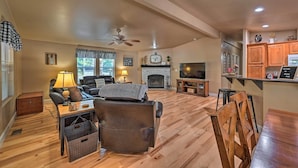 A spacious living room with a fireplace, a television, and a dining area with wooden furniture. - Near Hiking: Munds Park Cabin w/ Deck & Yard (Munds Park)