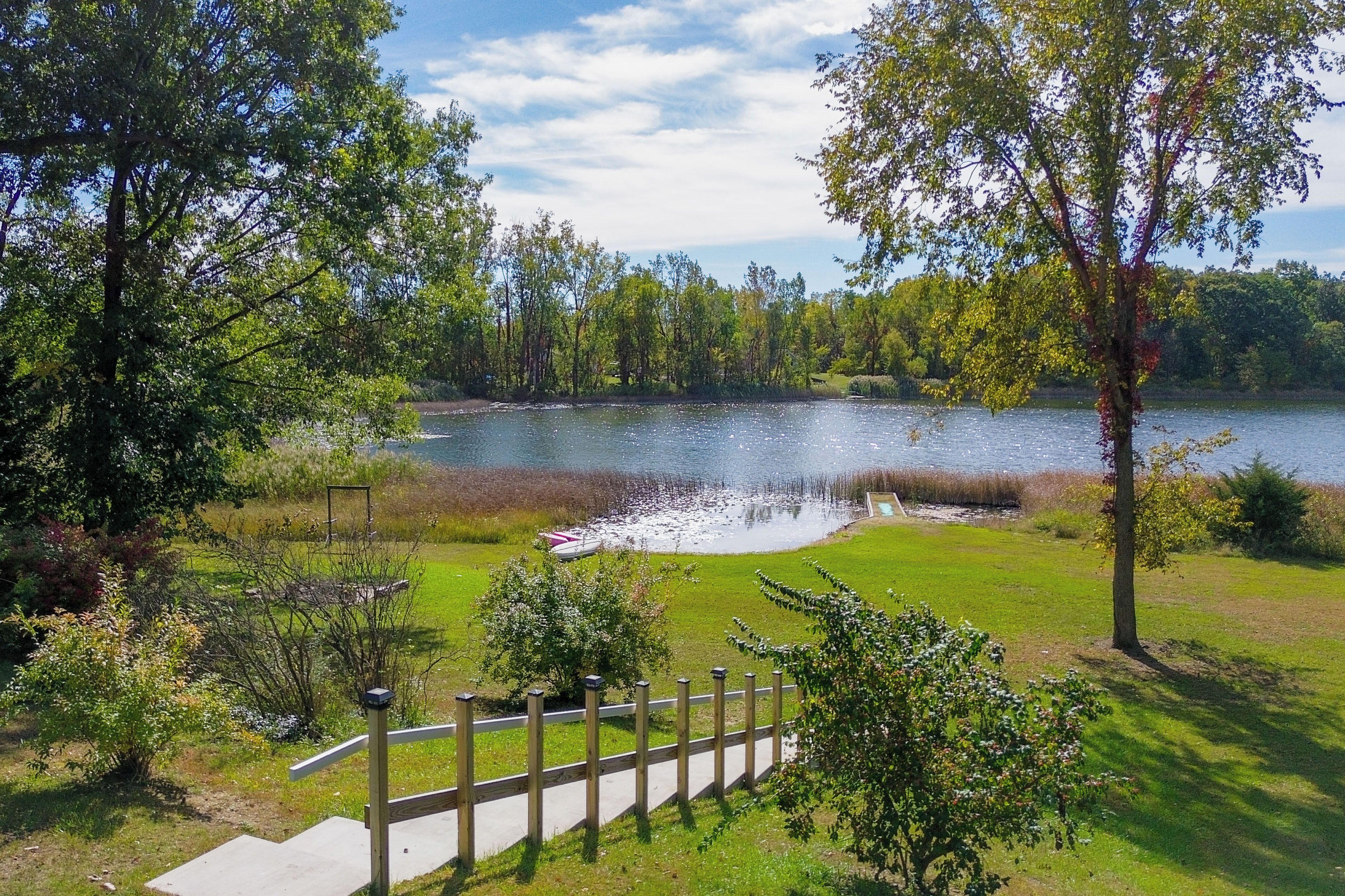 A lakeside view with a wooden deck, grassy areas, and trees.