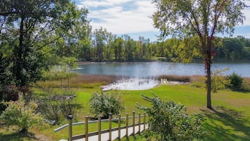 A lakeside view with a wooden deck, grassy areas, and trees.