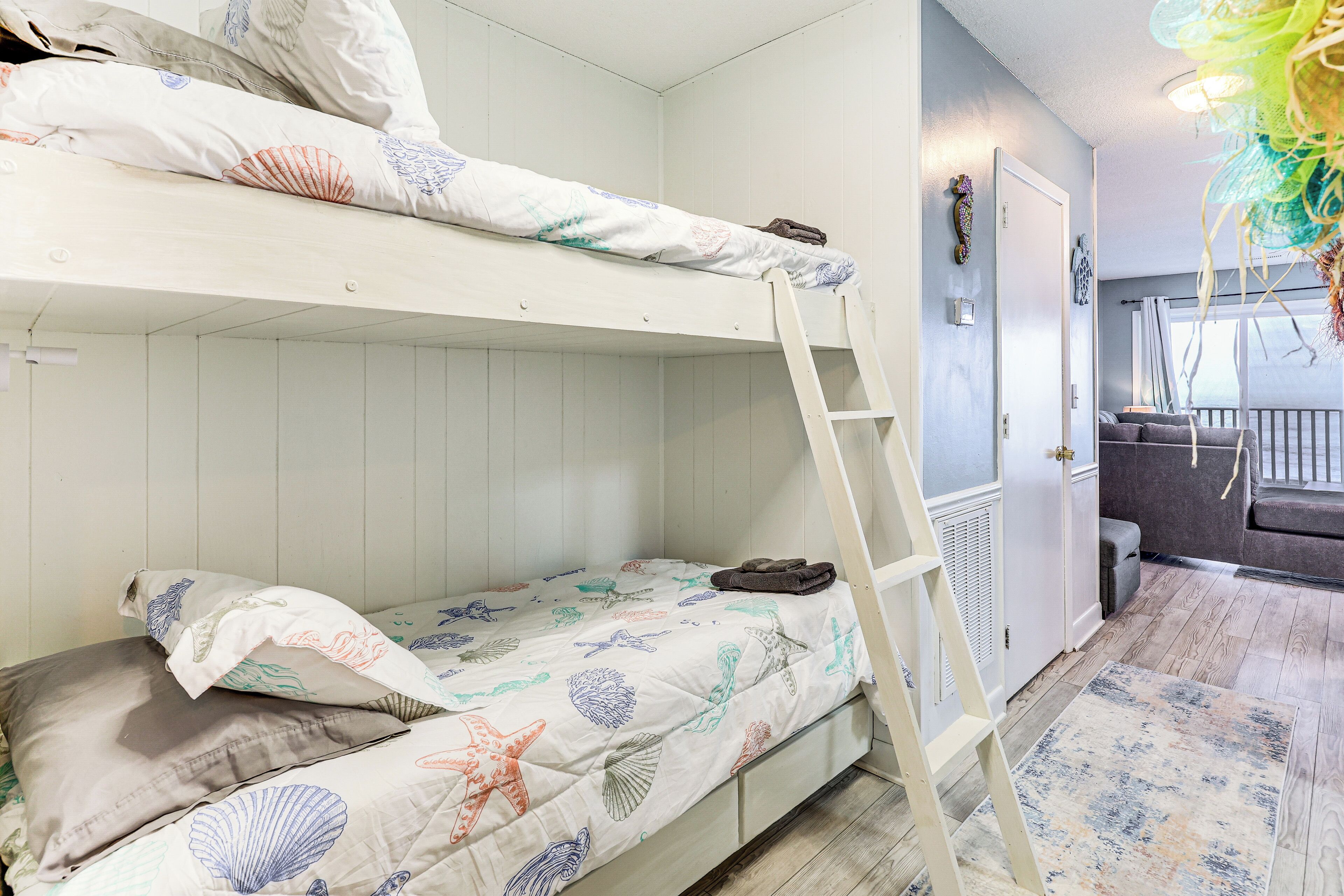 Een stapelbed met een ladder, een kleine bank en een kamer met houten vloeren en een patroonkleed.