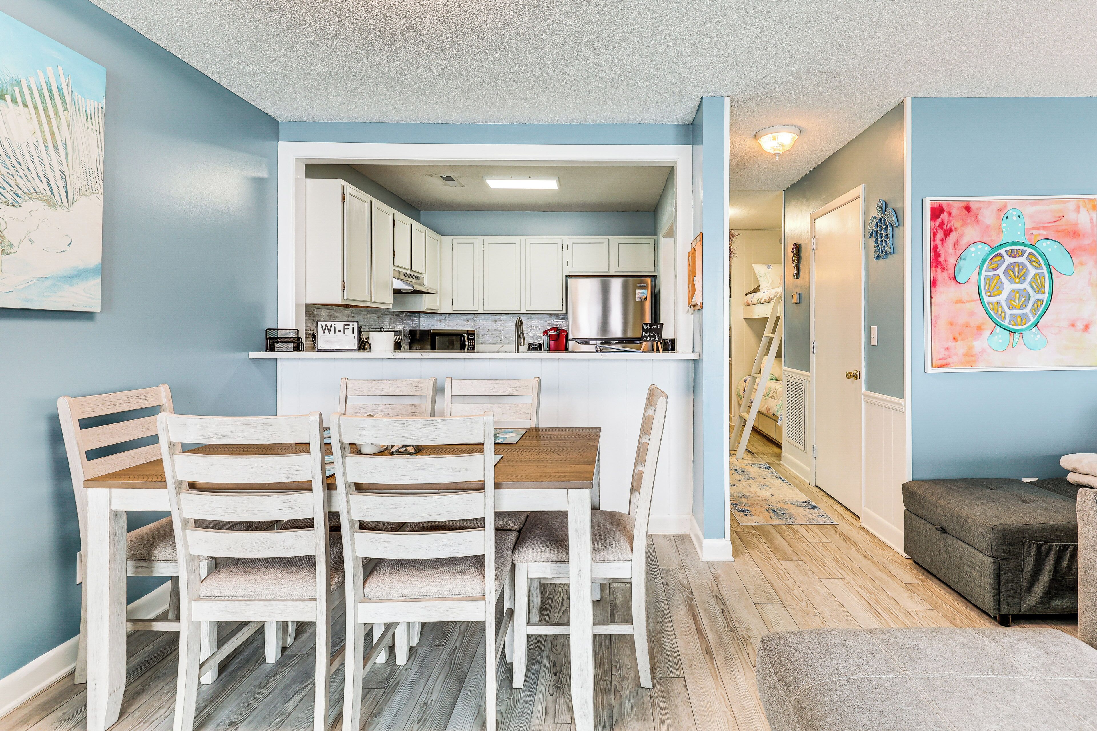 A modern kitchen with white cabinets, a stainless steel refrigerator, and a dining area with wooden chairs and a table.
