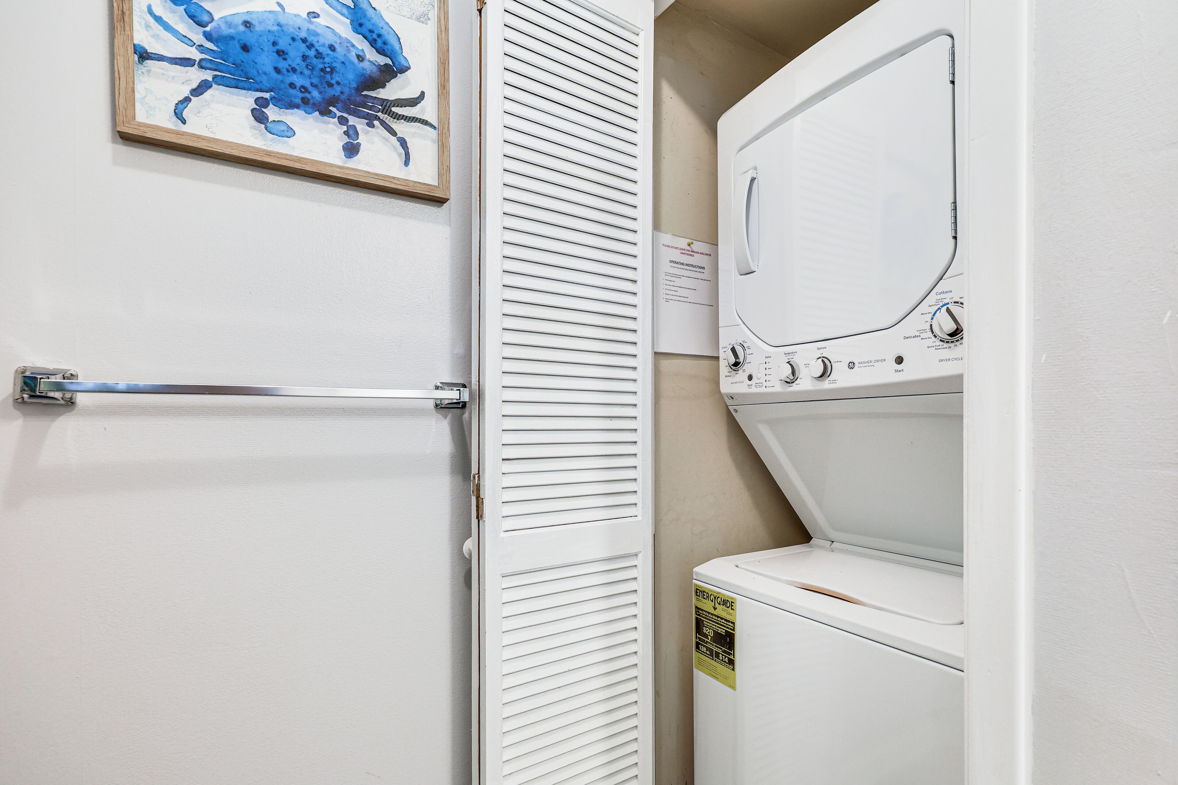 Een wasruimte met een witte wasmachine, een droogrek en een deur met een verstelbaar lamellenrooster.