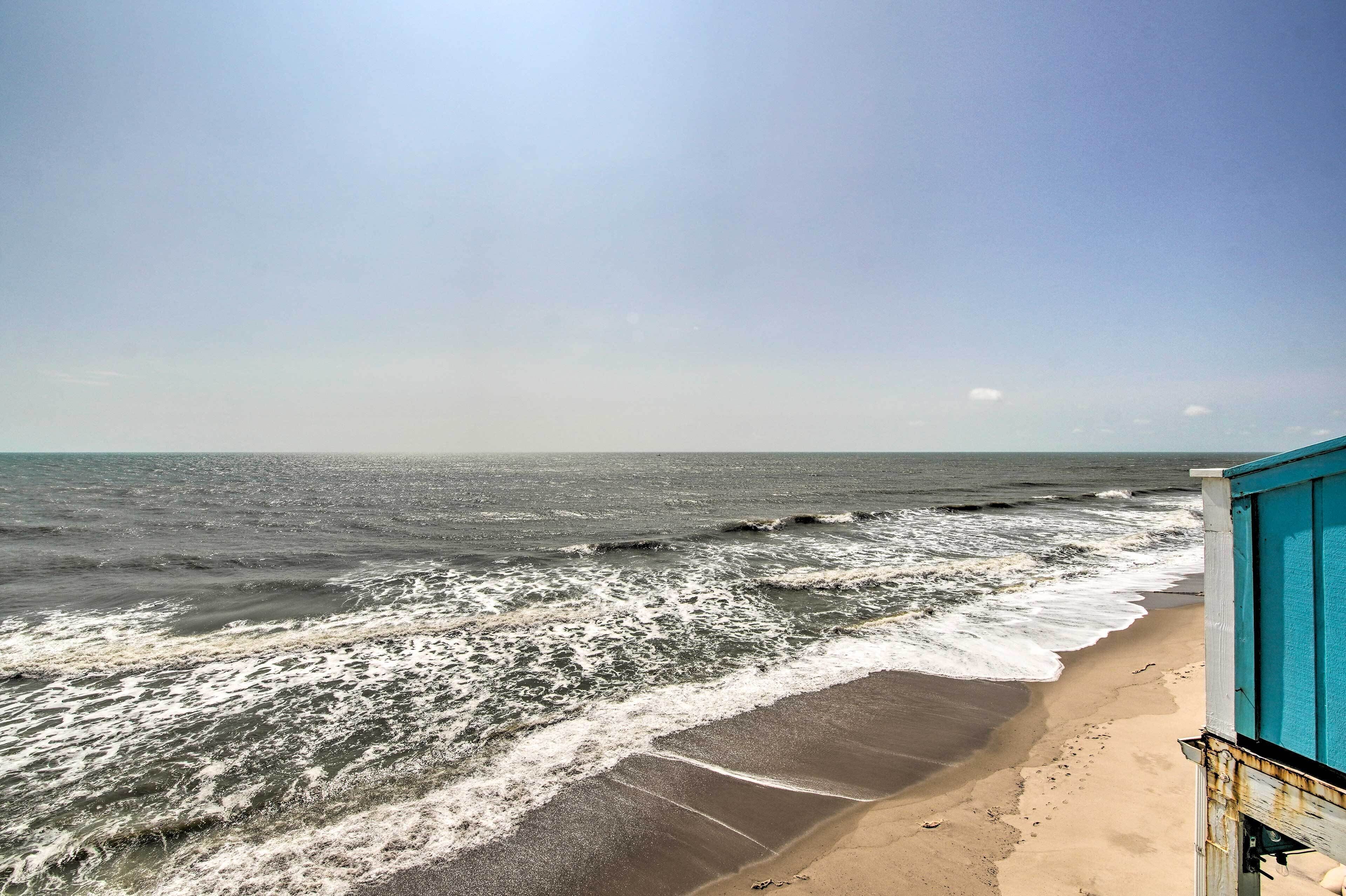 A beach with waves crashing onto the shore and a blue building in the foreground.