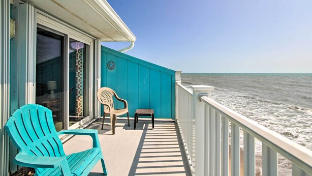 A balcony with a view of the ocean, a turquoise chair, a small stool, and a white railing. - Kure Beach Condo w/ Panoramic Ocean Views! (Kure Beach)
