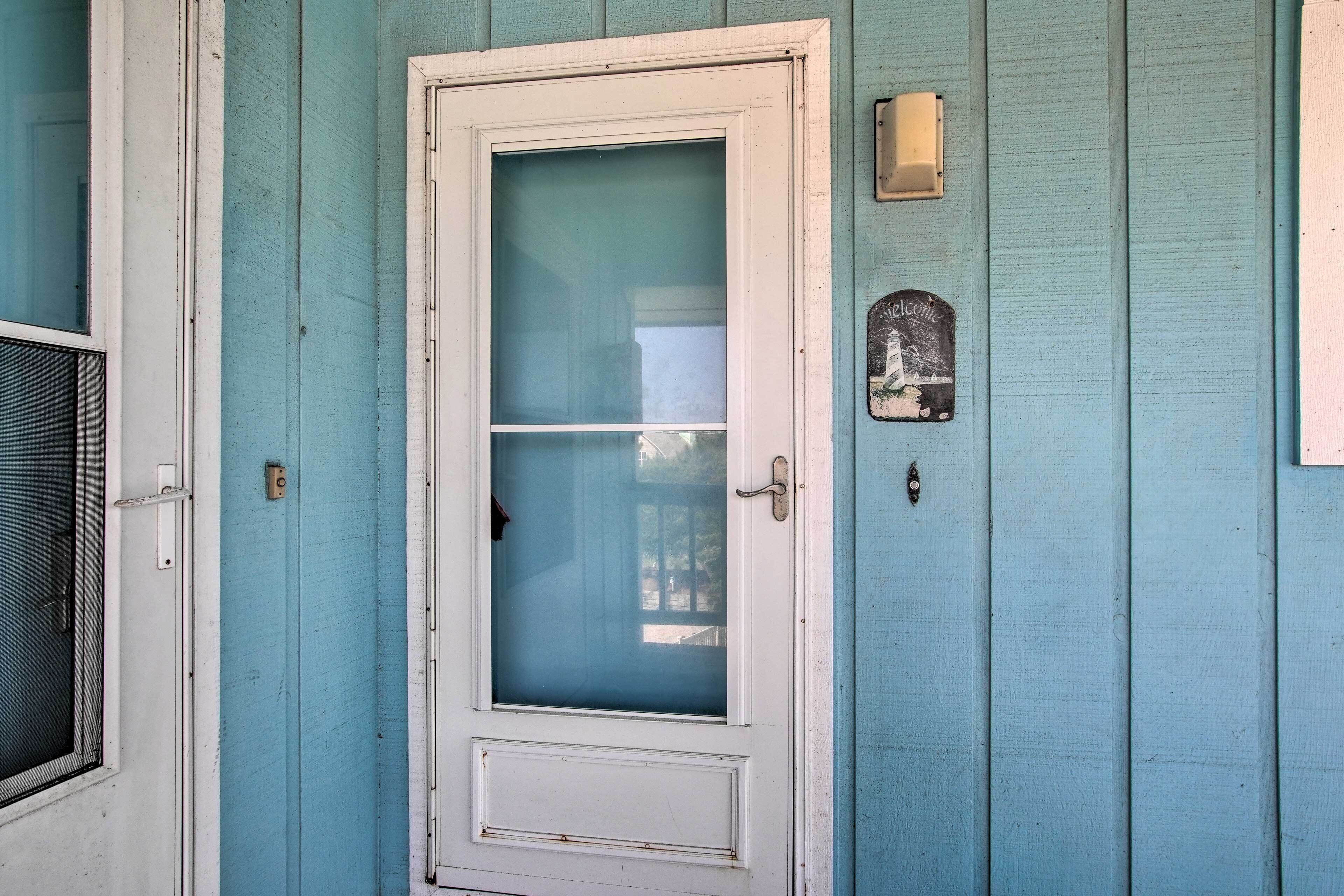 A white door with a frosted glass panel, a small mailbox, and a welcome sign on a teal-painted wall.