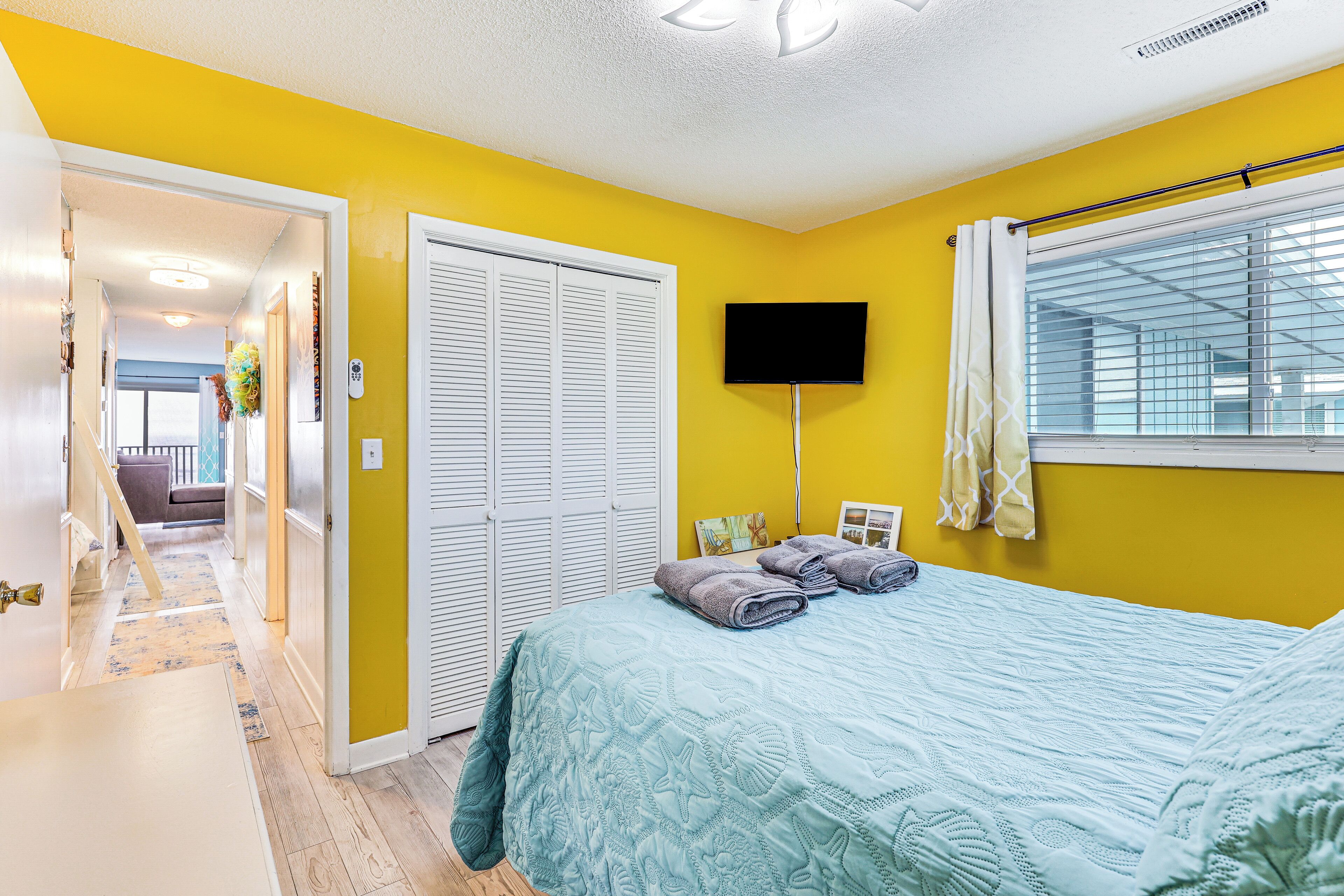 A bedroom with a bed, a TV, and a window with blinds.