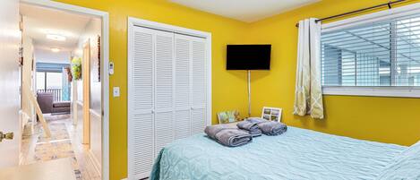 A bedroom with a bed, a TV, and a window with blinds.