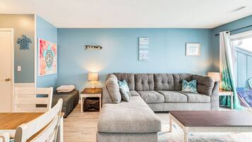 A living room with a grey sectional sofa, a wooden dining table, and a small side table with a lamp.