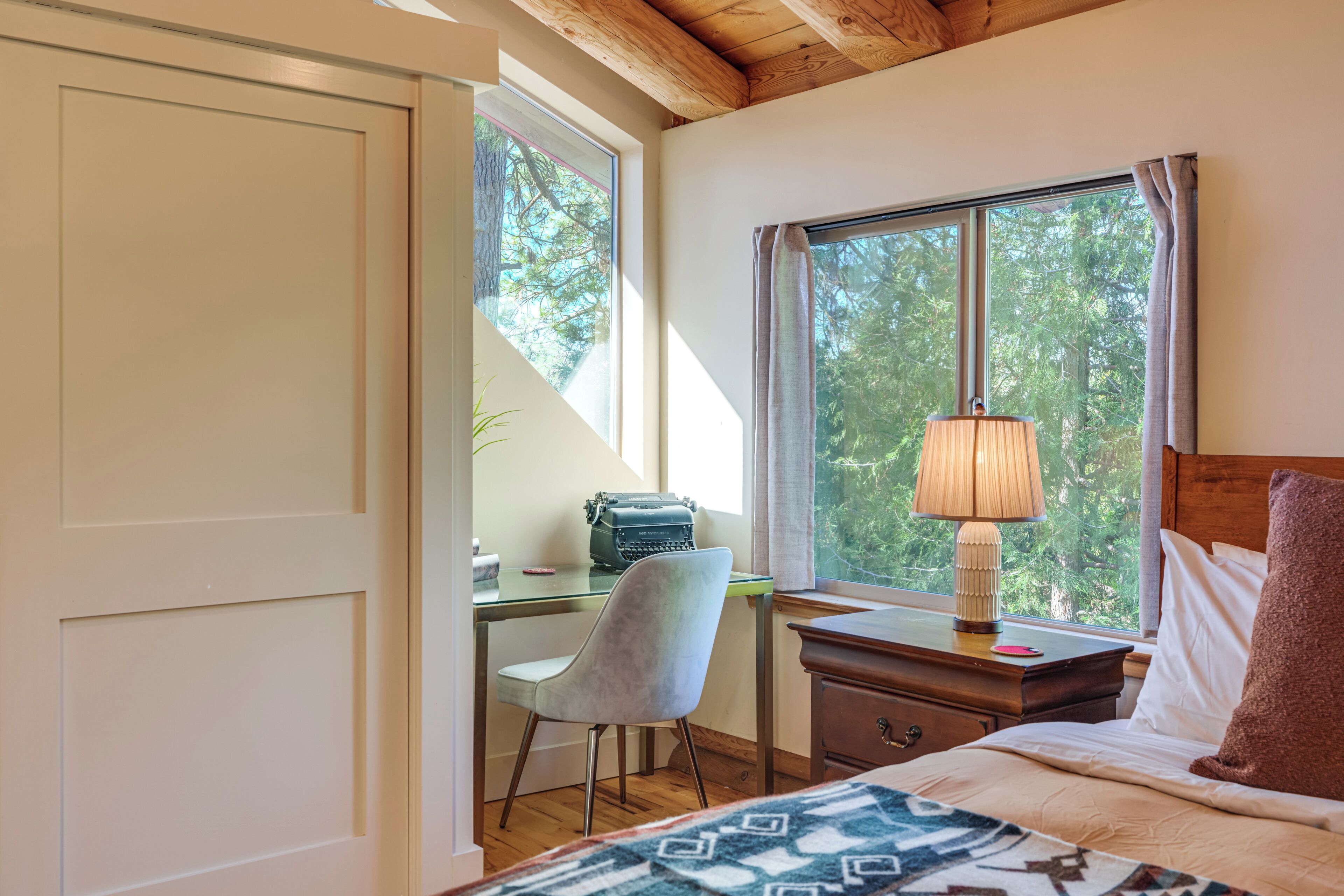 Une chambre à coucher avec un lit, un bureau avec une chaise, une lampe et une fenêtre avec des rideaux.