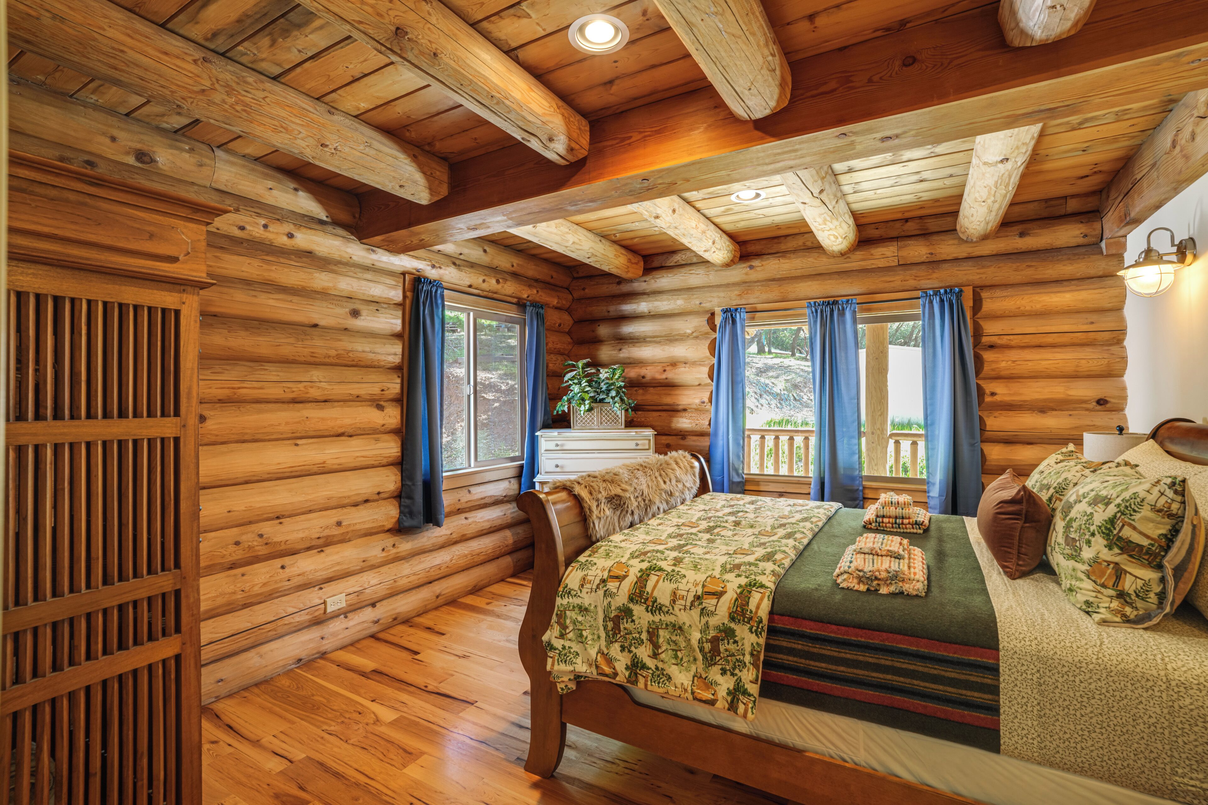 Una habitación estilo cabaña de troncos con una cama de madera, un aparador y una ventana con cortinas.