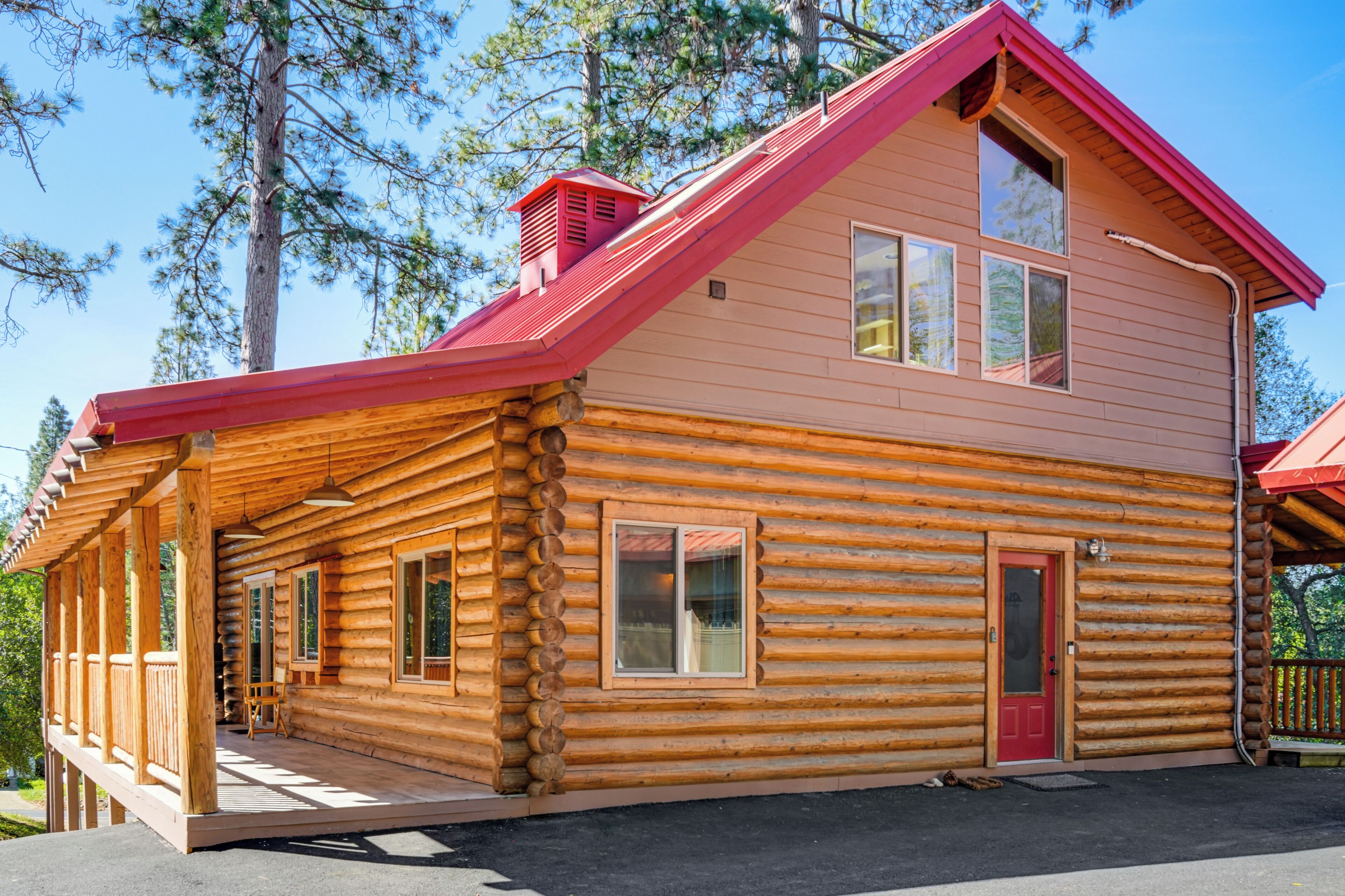Een vakantiehuis in blokhutstijl met een rood dak, grote ramen en een veranda.