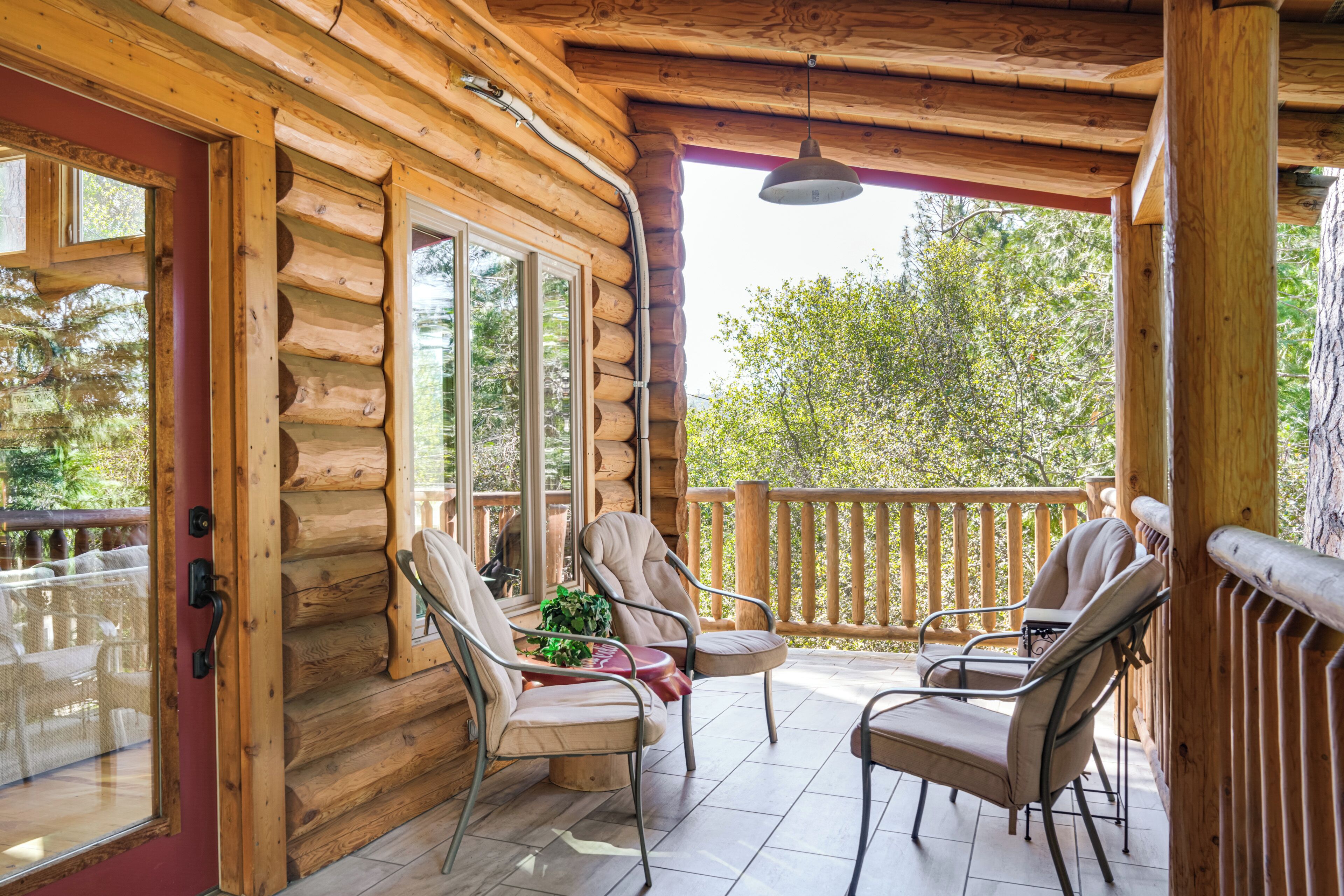 A log cabin with a wooden deck, two chairs, a table, and a hanging light fixture.