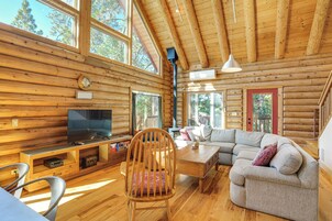 A log cabin interior with a wooden floor, a television, a sofa, a chair, and a staircase.