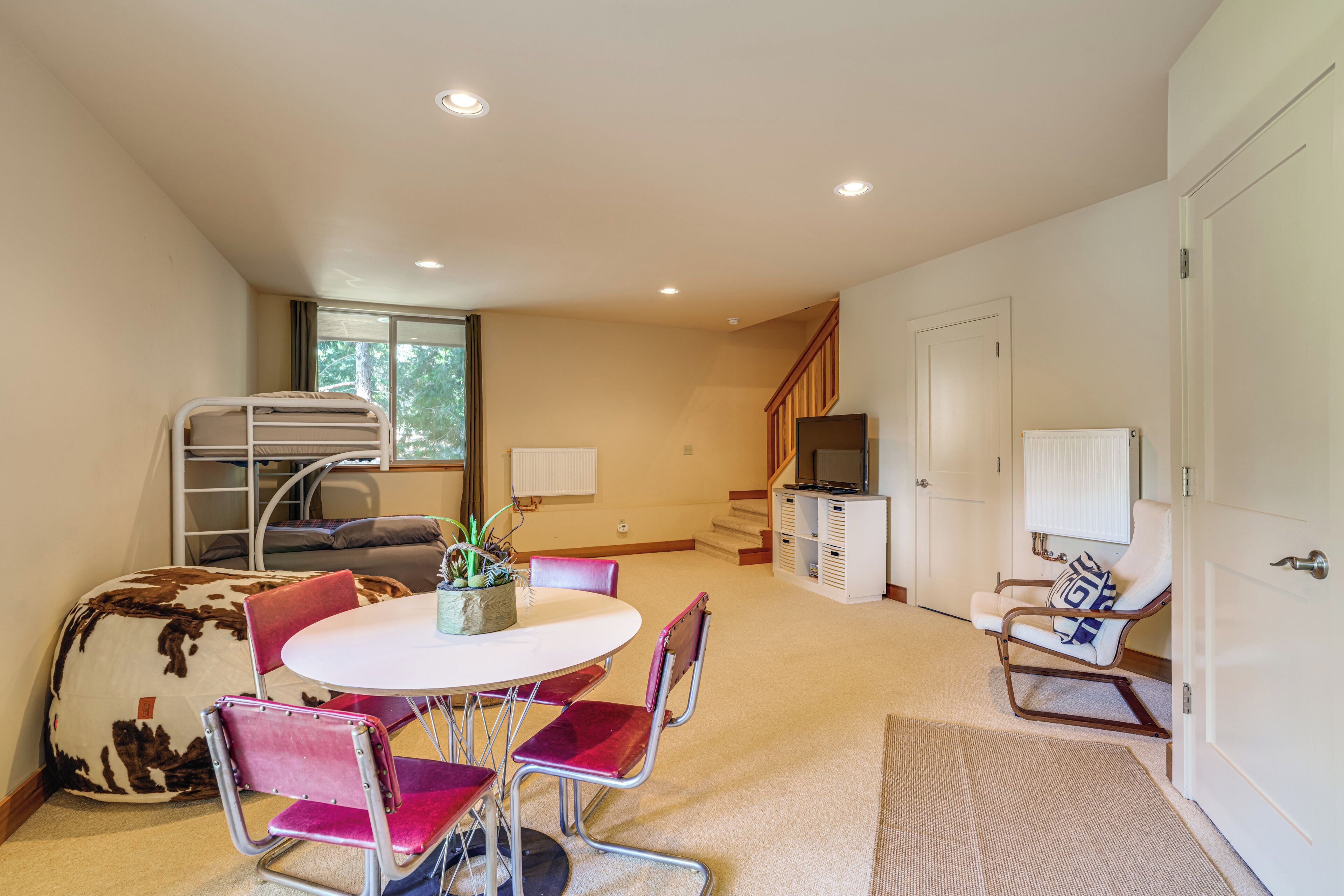 A compact living space with a bunk bed, a round table with chairs, a television, and a staircase leading to another level.