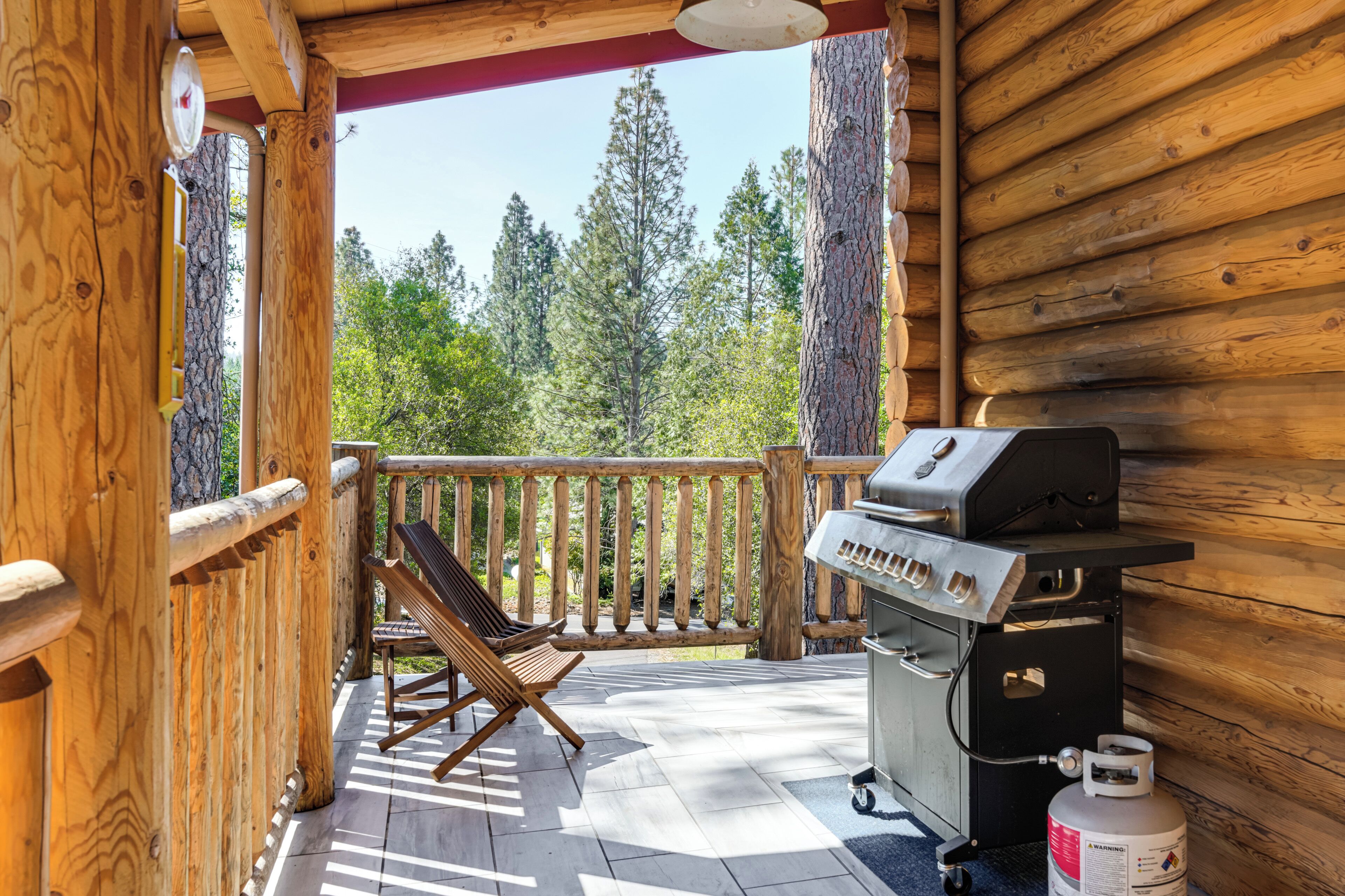 Una terraza de madera con una parrilla y una silla, con vista a un bosque.