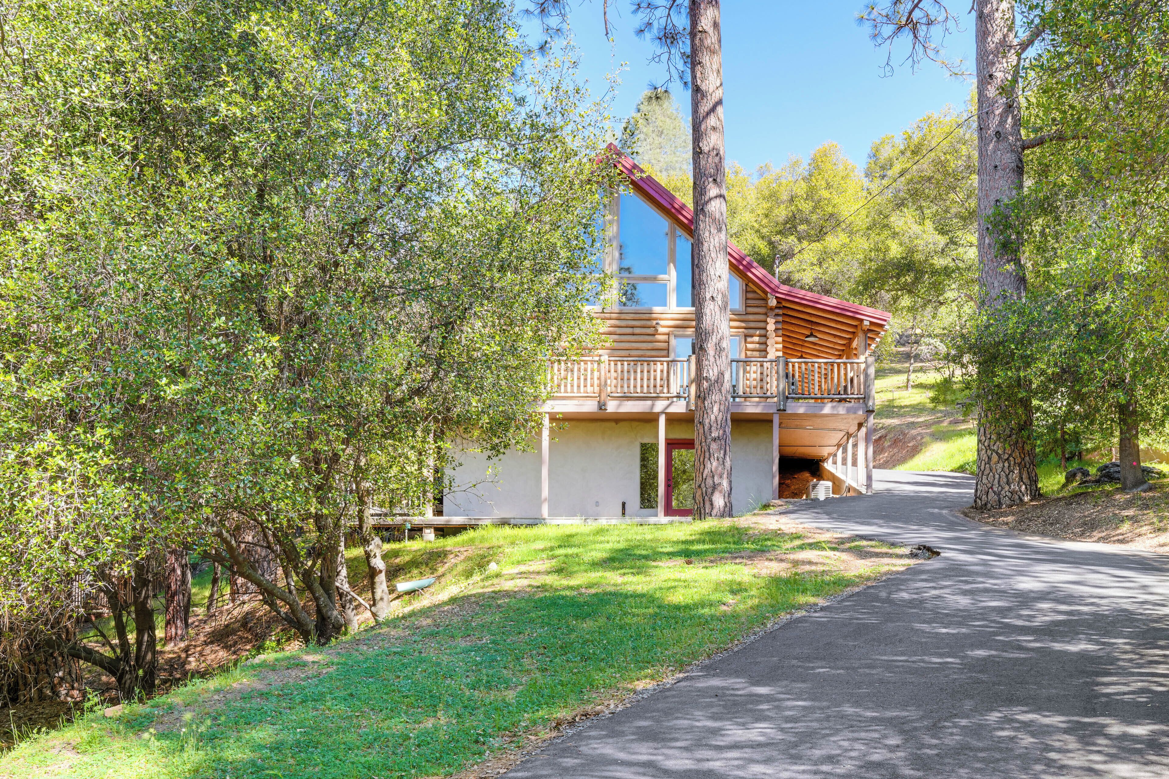 A cabin with a balcony, surrounded by trees, and a paved path leading to it.
