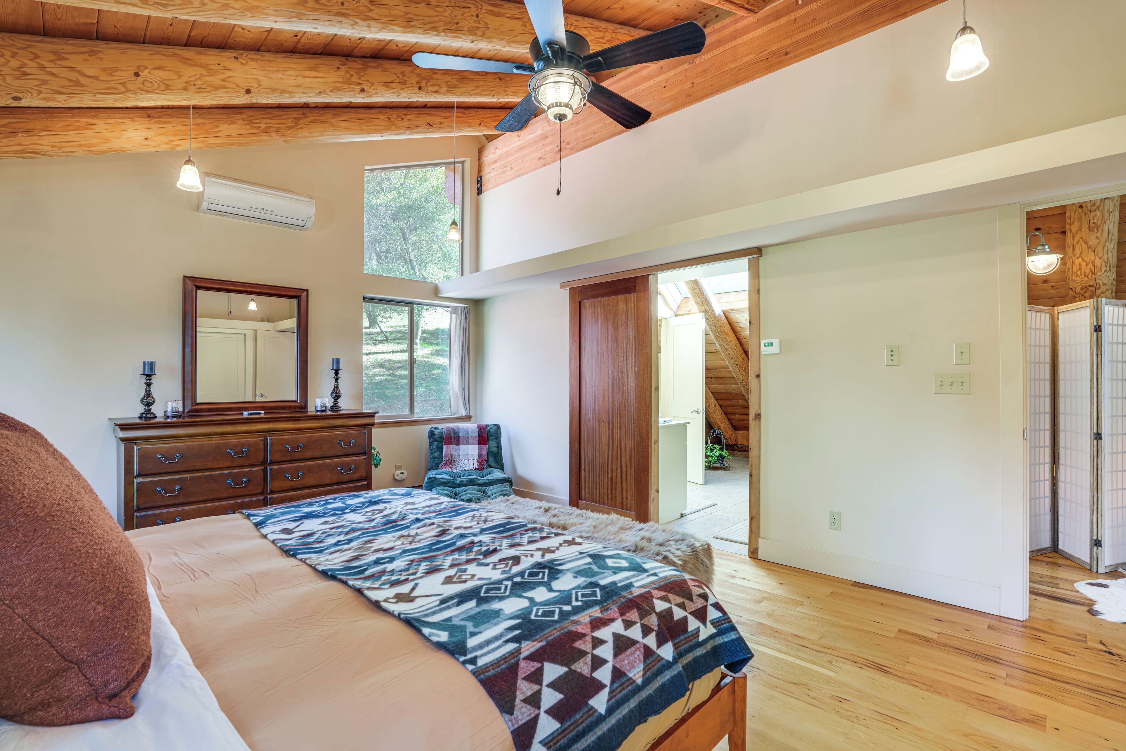A bedroom with a bed, dresser, mirror, ceiling fan, and wooden floors.