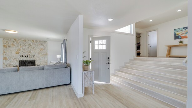 A modern living room with a stone fireplace, a grey sofa, and a staircase leading to another level. - Pool, Game Room, Hot Tub: Lake Havasu City Oasis! (Lake Havasu City)