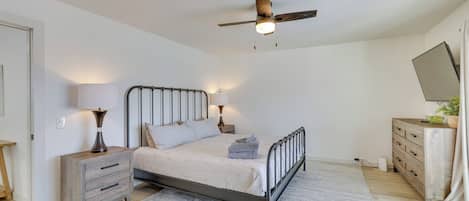 A bedroom with a bed, bedside lamps, a wooden nightstand, a dresser, a ceiling fan, and a mirror.