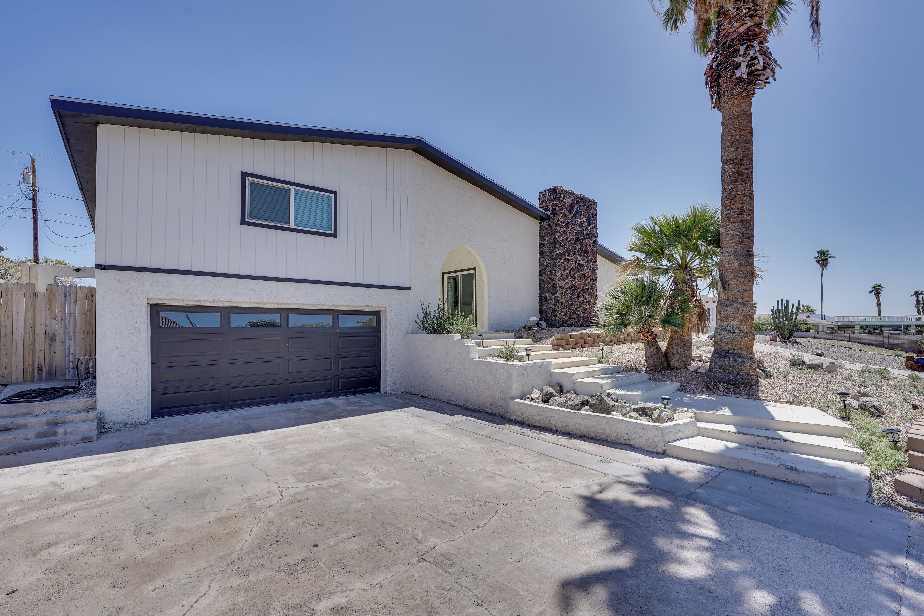 A modern two-story house with a garage, a stone fireplace, and a landscaped front yard with palm trees and rocks.